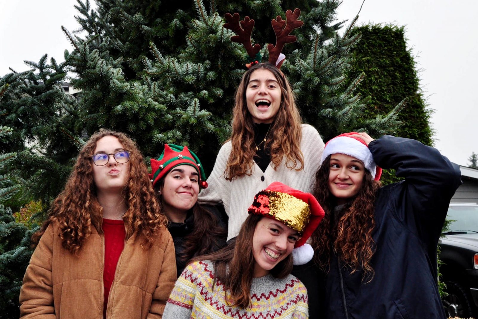 Cinco amigas portando gorros navideños, frente a árbol de navidad