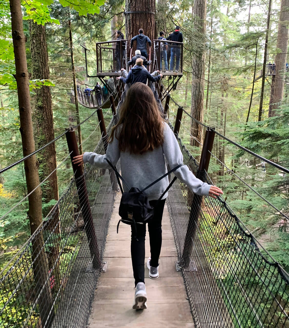 Chica adolescente y otros visitantes, caminando por puente aéreo entre las copas de los árboles