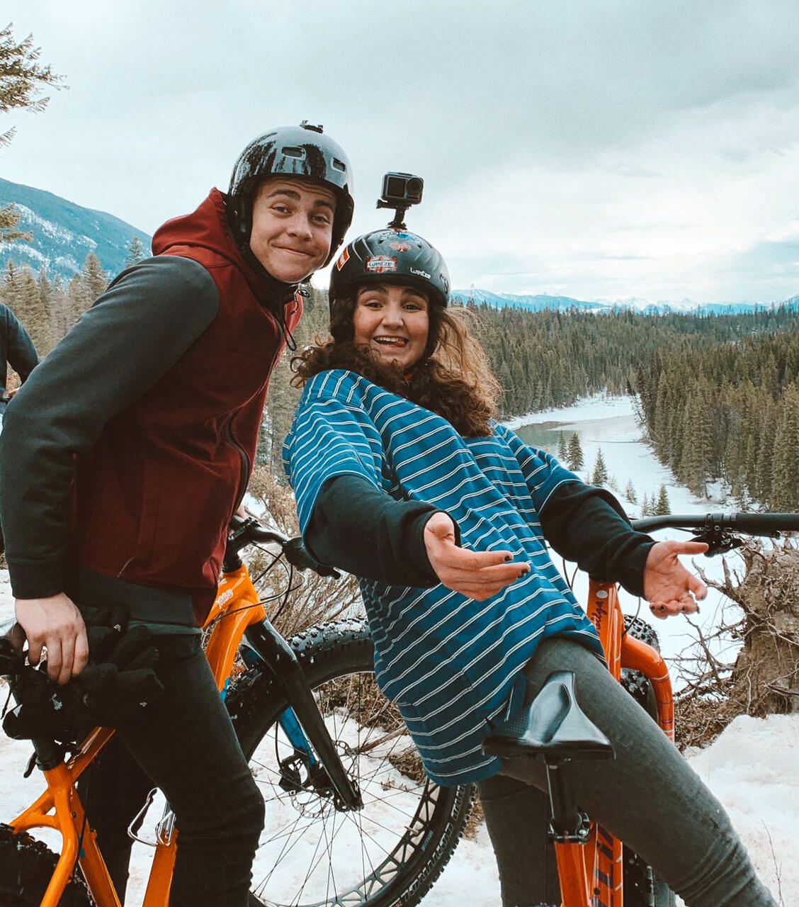 Dos estudiantes, portando bicis de montaña y cascos de protección con cámaras de Go-Pro en medio de un paisaje espectacular de bosque nevado