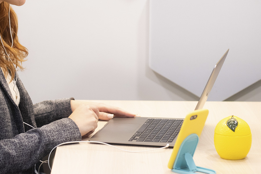 Asesor de The Lemon Tree Education utilizando un ordenador portátil y un teléfono móvil para comunicarse por videollamada, junto a un accesorio decorativo con forma de limón.