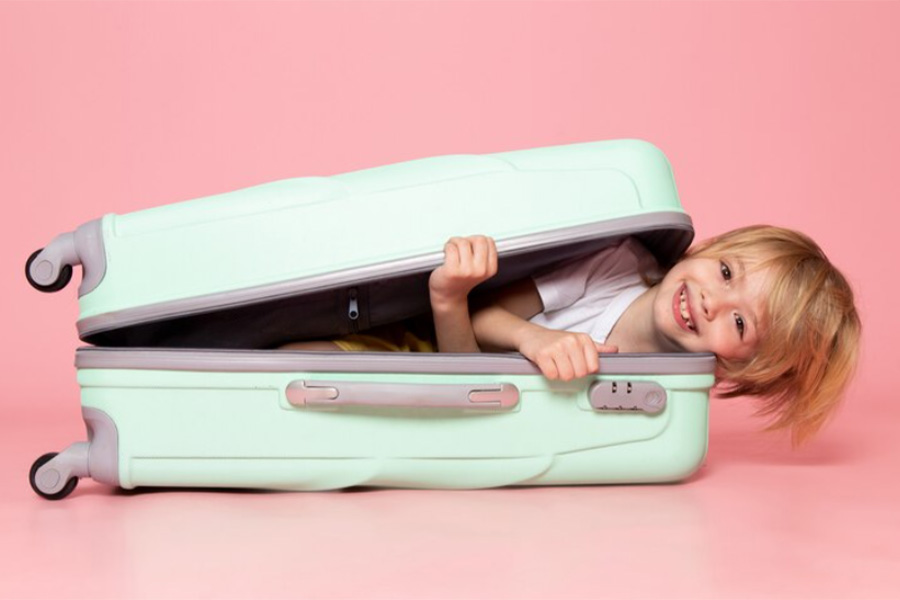 Primer plano de un niño feliz y sonriente asomando la cabeza desde el interior de una maleta de viaje verde.
