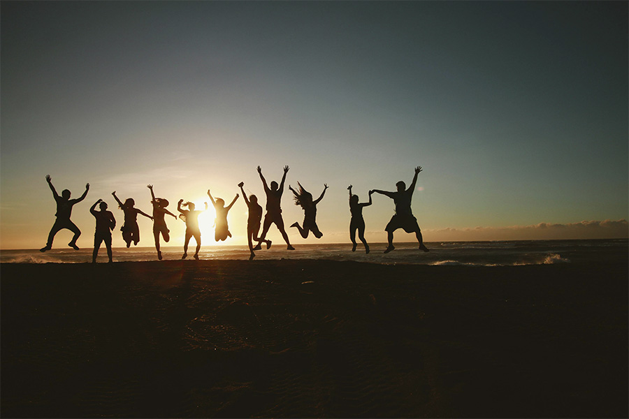 Grupo de amigos saltando en la playa frente al mar durante el atardecer, estilo silueta.