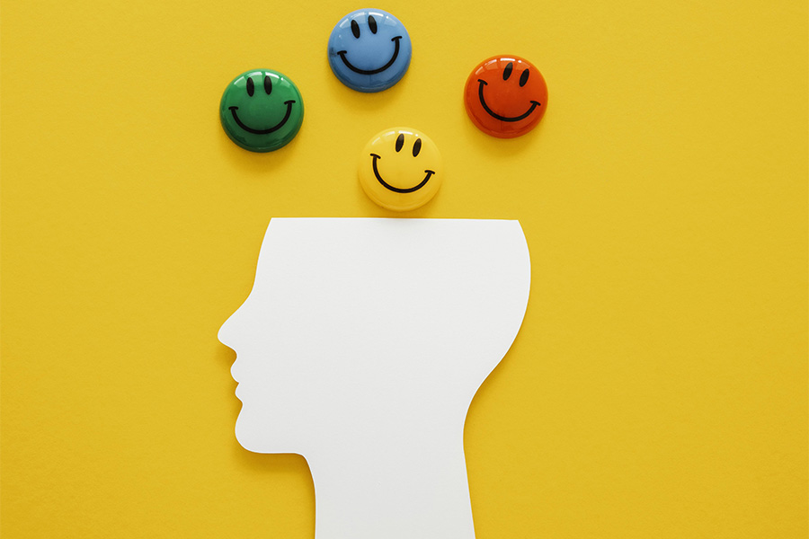 Perfil de cabeza humana con emoticonos de colores que representan emociones positivas y gratitud.