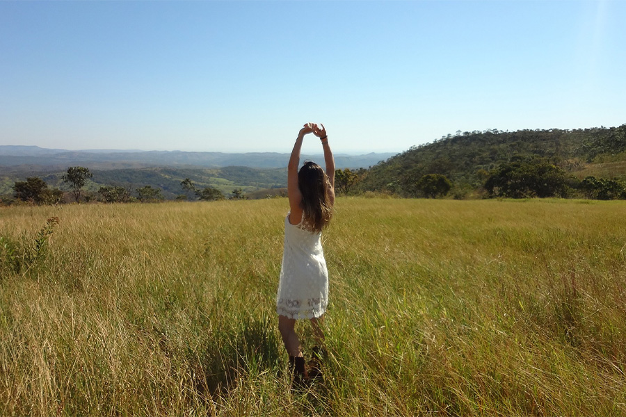 Mujer con los brazos levantados en un campo abierto bajo el sol, representando el equilibrio y bienestar personal.