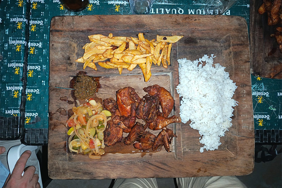 Plato de madera con comida típica de Costa de Marfil: pollo frito, arroz, patatas fritas y salsa.