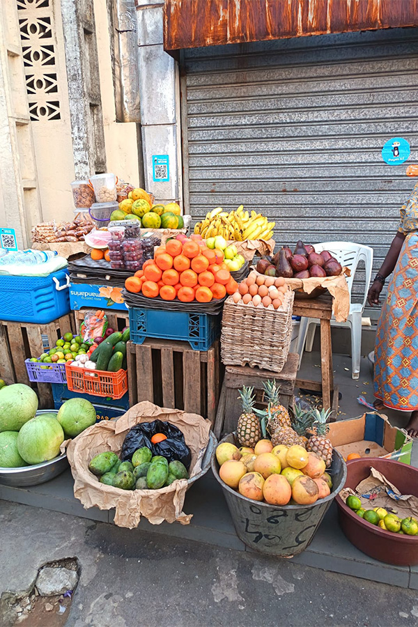 Puesto callejero colorido en Abiyán con frutas tropicales como mangos, piñas y naranjas.