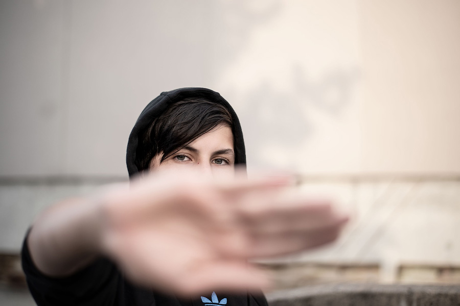 Retrato de una persona joven con capucha cubriendo parte de su rostro con la mano en un gesto de límite o timidez.