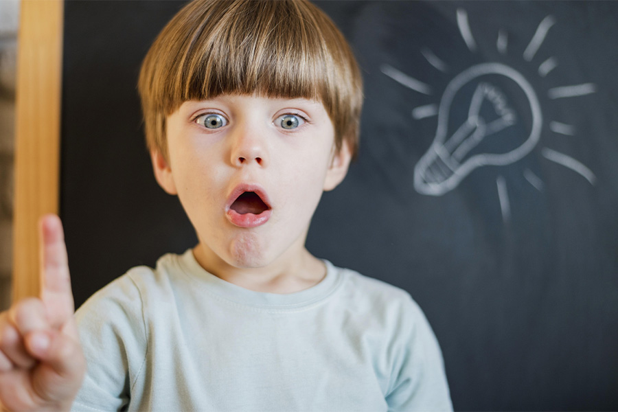 Niño sorprendido señalando una bombilla dibujada en una pizarra, simbolizando una idea o descubrimiento
