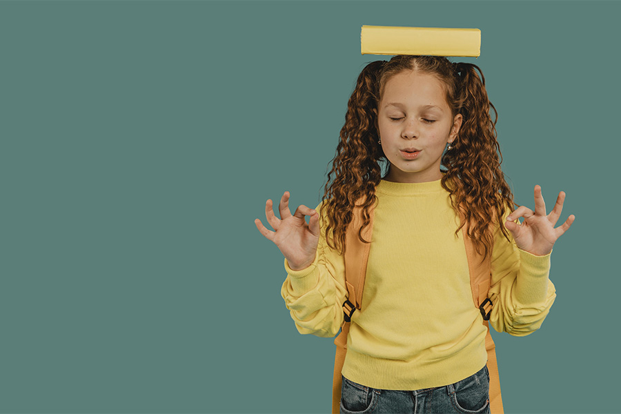Niña meditando con un libro en la cabeza buscando equilibrio y calma interior