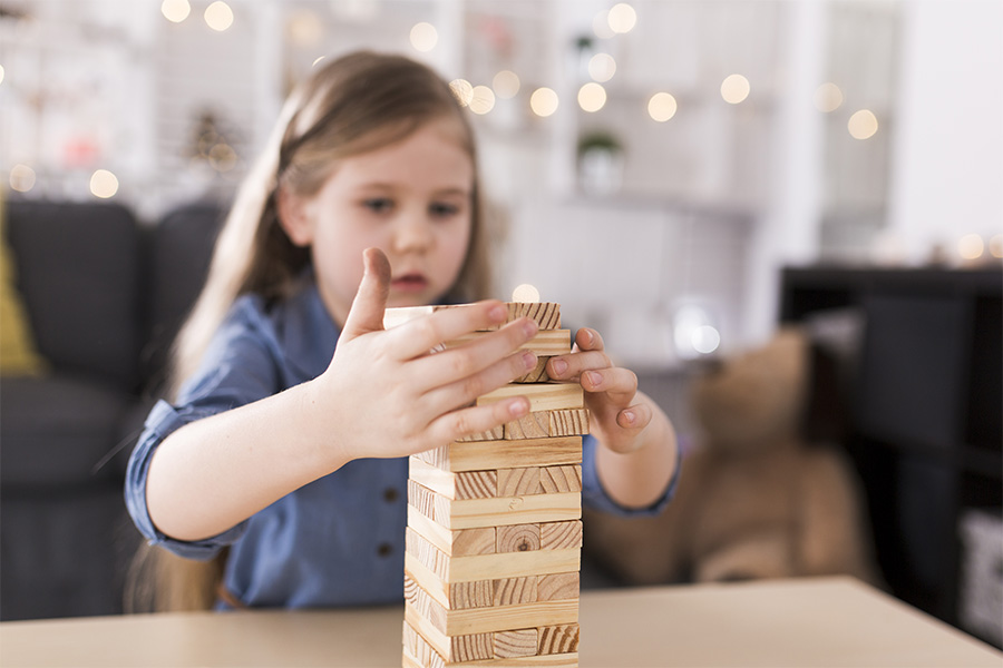 Niña pequeña concentrada construyendo una torre con piezas de madera.