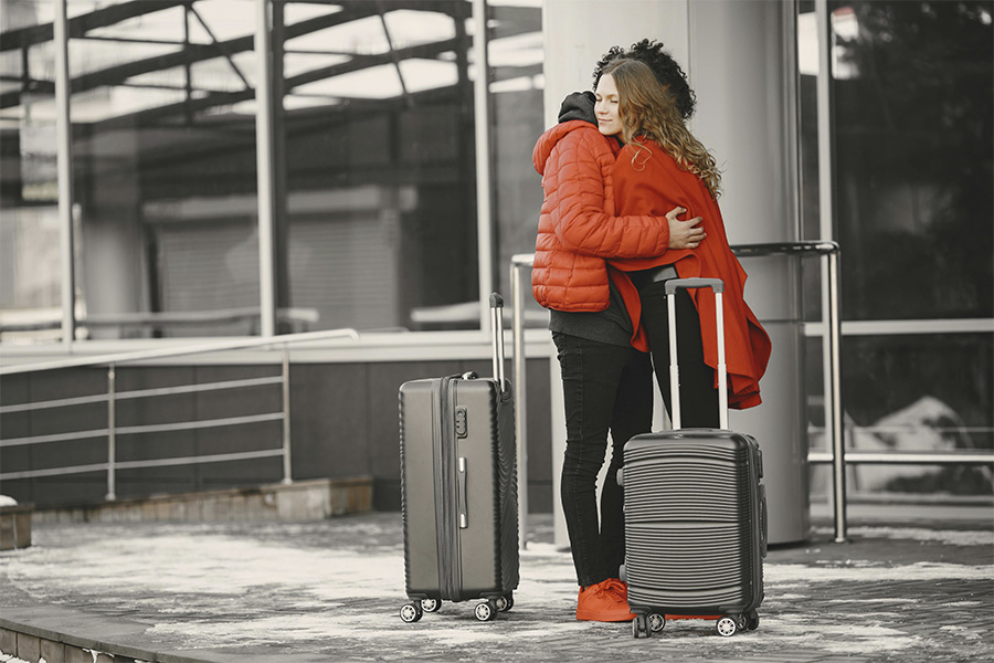 Pareja abrazándose junto a maletas negras frente a la terminal de cristal de un aeropuerto.