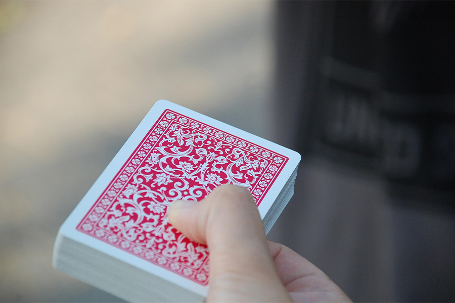 Primer plano de una mano sosteniendo una baraja de cartas con el reverso de patrón geométrico rojo, representando la comunicación indirecta.